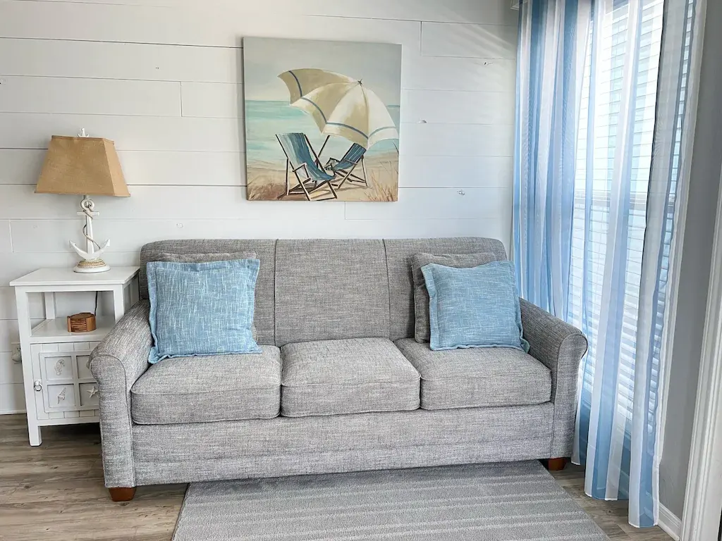Gray sleeper sofa with blue pillows and beach umbrella art at Seascape Condo 2208