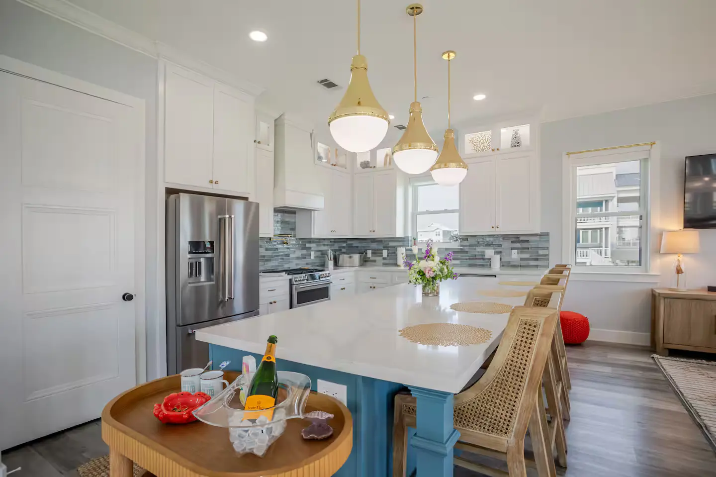 White kitchen with blue island, gold pendants, and rattan barstools at Alma de Mar